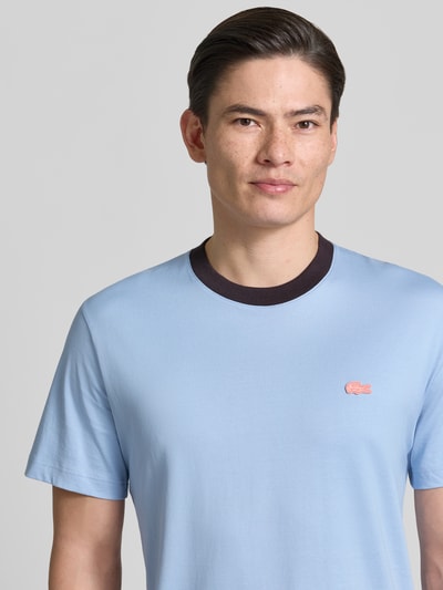 Männermodel trägt Regular Fit T-Shirt aus reiner Baumwolle von Lacoste in Optik: Unifarben mit Logo-Detail, Rundhals, Kurzarm, Jersey, Nahaufnahme Oberkörper.