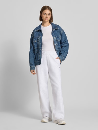 Kobiece model prezentuje Wide Fit Sweatpants aus reiner Baumwolle Modell 'Cassie' von Carhartt Work In Progress w kolorze jasnoszarym, wyhaftowane logo, elastyczny pas, długość wewnętrzna nogawki w rozmiarze S: 76 cm, bawełna, krój wide fit, całkowity widok z przodu.