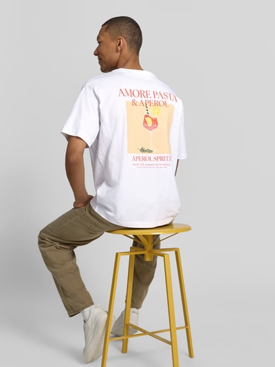 Männermodel trägt T-Shirt mit rückseitigem Motiv-Print von MCNEAL aus weißer Bio-Baumwolle und Statement-Print, Ganzkörperansicht Rückansicht.