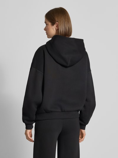 Frauenmodel trägt Hoodie mit Logo-Print und Känguru-Tasche von REVIEW, Baumwoll-Mix, schwarz, lockere Passform, Ganzkörperansicht Rückansicht.