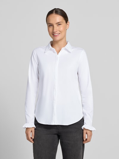 Kobiece modelka nosi białą bluzkę koszulową z mieszanki bawełny Model 'Mattie' od MOS MOSH, krój slim fit, rzędy guzików, falbany na zakończeniach rękawów, kołnierzyk koszulowy, zaokrąglony dół, długość tyłu 70 cm, długość rękawów 62 cm, widok całej sylwetki z przodu.