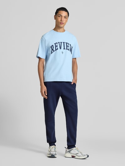 Męski model nosi Slim Fit Sweatpants aus Baumwoll-Mix von REVIEW, granatowy kolor, mieszanka bawełny, wpuszczane kieszenie, wyhaftowane logo, długość wewnętrzna nogawki 79 cm, krój slim fit, przód na całej długości, Ganzkörperansicht von vorne.