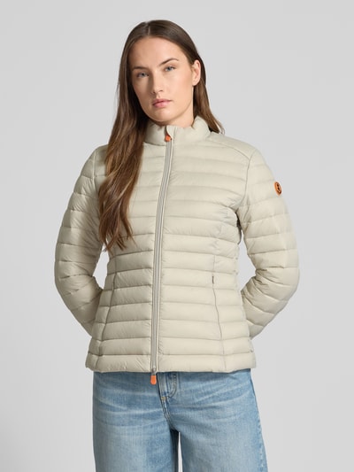 Frauenmodel trägt Slim Fit Steppjacke mit gefüttertem Stehkragen Modell 'Carly' von SAVE THE DUCK in Beige, horizontale Stepp-Optik, Reißverschlusstaschen, Ganzkörperansicht von vorne.
