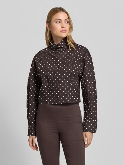 Frauenmodel trägt Kurze voluminöse Bluse - curated by Mary Braun von Style Icon Collection, braun mit weißen Punkten, Stehkragen, Regular Fit, reine Baumwolle, durchgehende Knopfleiste, Ganzkörperansicht von vorne.