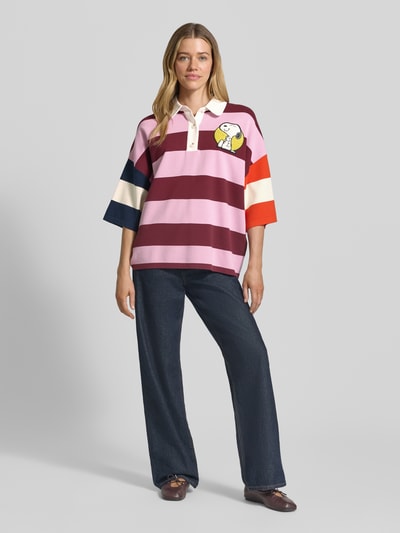 Kobiece model nosi koszulkę polo Oversized Poloshirt aus Viskose-Mix Modell 'JICE STRIPED EMBO' od Essentiel Antwerp, efekt: wielokolorowe paski, aplikacja z motywem, drobny splot, mieszanka wiskozy, krój oversized, rękaw o dł. 3/4, kołnierzyk polo, listwa guzikowa, wykończenie prążkowane, widok całej sylwetki z przodu.