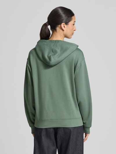 Modelka kobieca nosi Hoodie mit Tunnelzug Modell 'IMA' od MSCH Copenhagen w odcieniu zielonym, prosty krój, tył z kapturem, materiał z domieszką wiskozy i stretchu, kieszenie boczne, długie rękawy, widok całej sylwetki z tyłu.