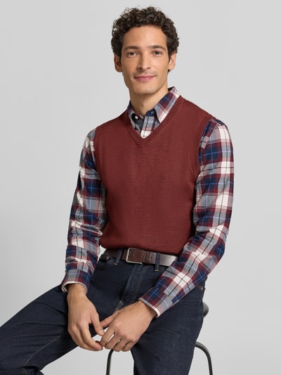 Mężczyznamodel nosi Slim Fit Pullunder aus Baumwoll-Mix mit V-Ausschnitt von Christian Berg Men, kolor bordowy, faktura dzianinowa, bezrękawnik, prążkowane wykończenia, bawełniany miks, długość tyłu w rozmiarze M: 73 cm, krój slim fit, widok na górną część ciała z przodu.