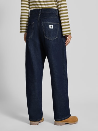 Vrouwenmodel draagt Wide Fit Jeans uit puur katoen Model "Brandon" van Carhartt Work In Progress, 5-pocketmodel, riemlussen, knoop- en ritssluiting, Bandwijdte maat S 41 cm, Binnenbeenlengte maat S 73 cm, donkerblauw, grove denimstructuur, Ganzkörperansicht Rückansicht.