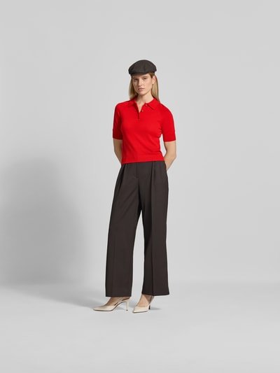 Frauenmodel trägt rotes Poloshirt aus reiner Wolle von Victoria Beckham, Regular Fit, Polokragen, Halbarm, Strick-Optik, schwarze Hose, Ganzkörperansicht von vorne.