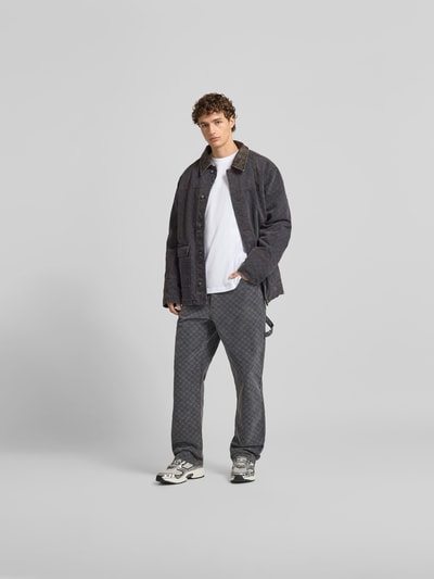 Männermodel trägt Jacke mit echtem Rindsleder-Besatz von DAILY PAPER aus Baumwolle, Relaxed Fit, dunkle Farben, Ganzkörperansicht von vorne.