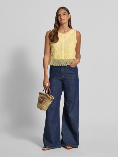 Frauenmodel trägt Regular Fit Top mit Lochstitching von Apricot in Gelb, reine Baumwolle, ärmellos, Rundhalsausschnitt, Zierschleife, kombiniert mit weiter Jeans, Ganzkörperansicht von vorne.