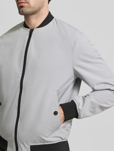 Männermodel trägt Regular Fit Bomberjacke mit Stehkragen von MCNEAL in Hellgrau mit schwarzen Bündchen, seitlichen Eingrifftaschen, Nahaufnahme Oberkörper. Elastischer Material-Mix, Reißverschluss, Regular Fit, Rückenlänge 70 cm, Schulterbreite 47 cm, Brustweite 55 cm, Ärmellänge 66 cm.