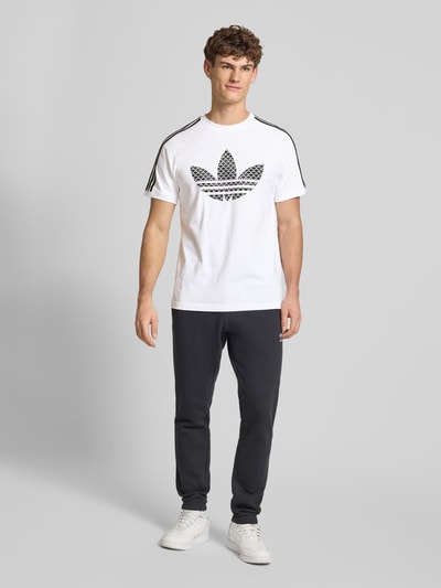Męski model nosi T-Shirt mit Label-Stitching od adidas Originals, biały kolor, bawełna, regular fit, prążkowany dekolt, cała sylwetka z przodu.
