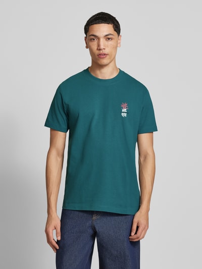 Männermodel trägt Relaxed Fit T-Shirt aus reiner Baumwolle von Marc O'Polo Denim in Petrol, unifarben mit Label- und Motiv-Print, Rundhals, Heavy Rough Jersey, Ganzkörperansicht von vorne.