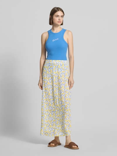 Frauenmodel trägt Maxi-Rock aus reiner Viskose Modell 'BARRI' von Pieces mit Optik:Allover-Muster, Passform: Schmal, Maxi-Länge, Bundabschluss: Elastisch, Material: Reine Viskose, in Gelb, Weiß und Blau mit zartem, leichtem Stoff, Ganzkörperansicht von vorne.
