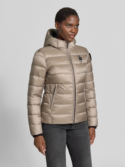 Modelka prezentuje kurtkę puchową z efektem pikowania z detalem z logo Model 'Charme' od Blauer USA, taliowany krój, kaptur, zamek błyskawiczny dwustronny, długość tyłu w rozmiarze S: 62 cm, szerokość ramion w rozmiarze S: 44 cm, szerokość w rozmiarze S: 43 cm, długość rękawów w rozmiarze S: 62 cm, jasny beż, matowa tekstura, widok całej sylwetki z przodu.