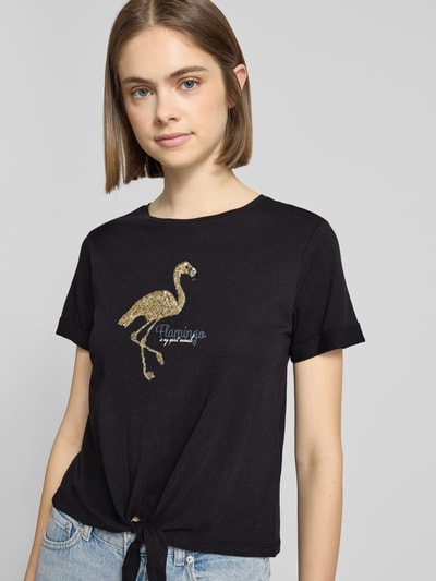 Frauenmodel trägt Regular Fit T-Shirt aus reiner Baumwolle Modell 'DORA LIFE' von Only in Schwarz mit Pailletten-Flamingo, Knotendetail, Rundhalsausschnitt, unifarbene Optik, kurzarm; Nahaufnahme Oberkörper.