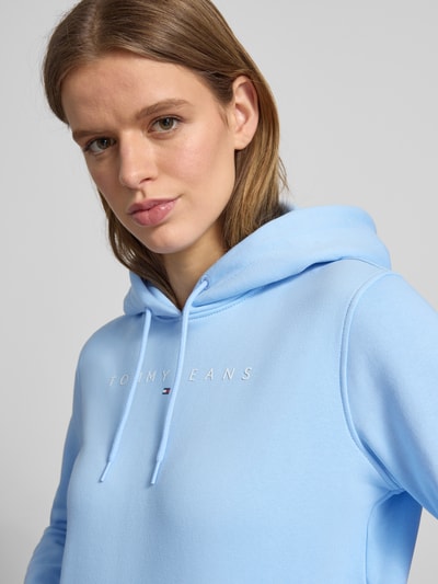Frauenmodel trägt Regular Fit Hoodie aus Baumwoll-Mix von Tommy Jeans in Hellblau, unifarben mit Label Print, Nahaufnahme Oberkörper.