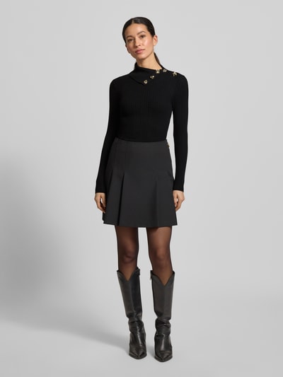 Frauenmodel trägt Slim Fit Rollkragenpullover aus Viskose-Mix Modell 'Sicilla' von Guess, Schwarz, Strick-Optik, Zierbesatz, Ganzkörperansicht von vorne.