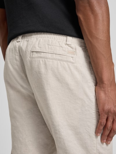 Männermodel trägt Regular Fit Leinenhose aus Leinen-Mix Modell 'SANDERSON' von BOSS Orange in Beige, Detailaufnahme Rückansicht. Material mit Flammgarn-Struktur, Gesäßtasche mit Label Patch, elastischer Bund und Tunnelzug.