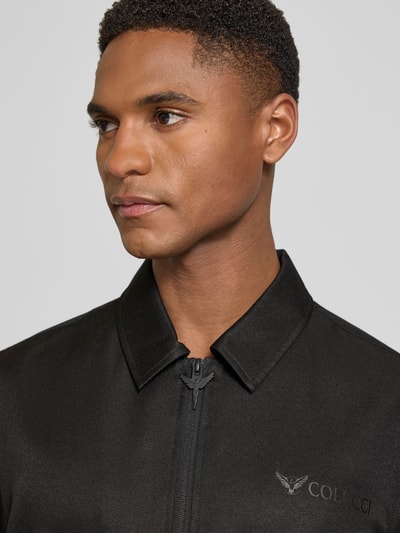Mannelijk model draagt Relaxed Fit vrijetijdsoverhemd met ritssluiting van COLUCCI, zwart, gestikt logo, platte kraag, met korte mouwen, Nahaufnahme Oberkörper.