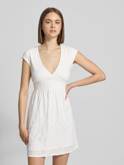 Frauenmodel trägt Kurzes Kleid mit V-Ausschnitt, Lochstickerei und großer Schleife von REVIEW, weißer Material-Mix mit Stretch-Anteil, A-Linie, Allover-Lochstickerei, Nahaufnahme Oberkörper.