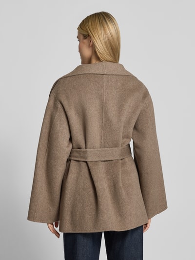Frauenmodel trägt Kurzblazer aus Woll-Mix mit Bindegürtel von COMMA, beige Farbe, lockere Passform, Rückenansicht, Ganzkörperansicht Rückansicht. Rückenlänge 76 cm, Schulterbreite 48 cm, Brustweite 57 cm, Ärmellänge 58 cm, Regular Fit, mit breitem Umlegekragen und Eingrifftaschen.