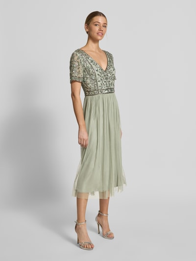 Frauenmodel trägt Knielanges Kleid mit floralem Pailettenbesatz von LACE & BEADS in zartem Grün, tailliert, V-Ausschnitt, Mesh, Kurzarm, Ganzkörperansicht von vorne.