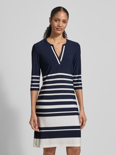 Modelka nosi Knielanges Kleid mit V-Ausschnitt von Christian Berg Woman Selection, mieszanka materiałów z dodatkiem streczu, taliowany krój, długość do kolan, dekolt w serek, rękaw o dł. 3/4, długość tyłu w rozmiarze 36: 92 cm, szerokość w rozmiarze 36: 44 cm, długość rękawów w rozmiarze 36: 43 cm, ciemnoniebieskie i białe poziome pasy, gładka tekstura, widok całej sylwetki z przodu