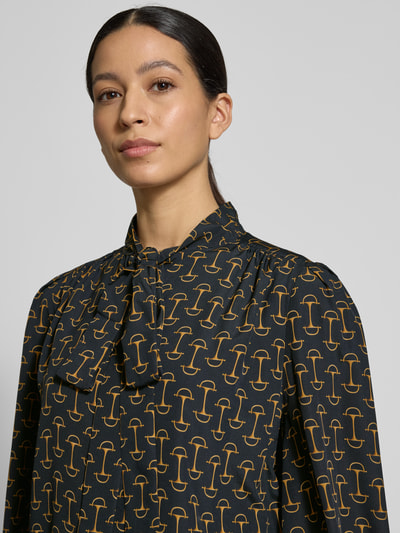 Frauenmodel trägt Regular Fit Langarmbluse mit Allover-Muster Modell 'KLARYCE' von Lauren Ralph Lauren in Dunkelblau mit goldfarbenem Muster, Stehkragen mit Bindeschleife, Satin-Optik, Nahaufnahme Oberkörper.