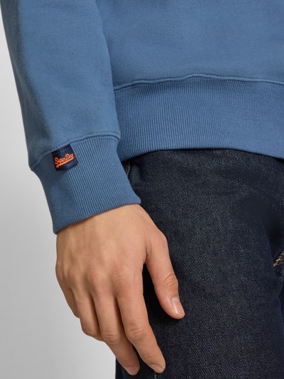 Männermodel trägt sweatshirt mit ronde hals en labelstitching van Superdry in katoenmix, regular fit, detailaufnahme onderarm.