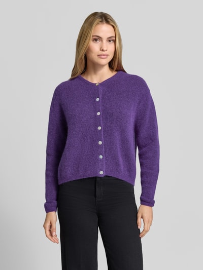 Frauenmodel trägt Relaxed Fit Strickjacke aus Woll-Mix mit Leinen-Anteil von American Vintage, lila Farbe, gerippte Bündchen, Knopfleiste, Langarm, Damen Strickjacke, Ganzkörperansicht von vorne.
