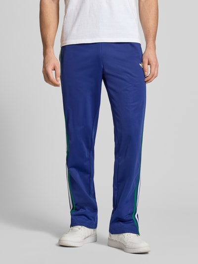 Männermodel trägt Regular Fit Sweatpants mit mehrfarbigen Kontraststreifen Modell 'FIREBIRD TP' von adidas Originals, unifarben, Logo-Stitching, elastischer Bund, Reißverschlusstaschen, Ganzkörperansicht von vorne.