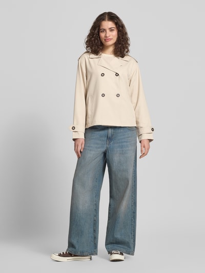 Frauenmodel trägt Regular Fit Trenchcoat-Jacke mit Reverskragen Modell 'HANNAH' von Only in Beige, doppelreihige Knopfleiste, Schulterriegel, langarm, seitliche Eingrifftaschen, unifarbene Optik, Ganzkörperansicht von vorne.
