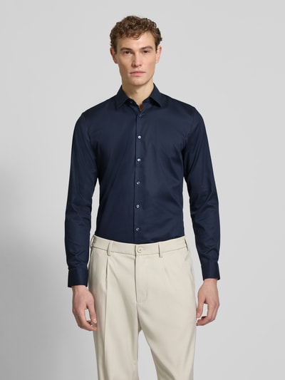 Męski model nosi Slim Fit Businesshemd mit Kentkragen von OLYMP No. Six, ciemnogranatowy, elastyczny bawełniany materiał, długi rękaw, krój slim fit, sportowe mankiety, guziki na całej długości, widok całej sylwetki z przodu. Długość pleców w rozmiarze 40: 81 cm, szerokość ramion w rozmiarze 40: 43 cm, długość rękawa w rozmiarze 40: 67 cm.