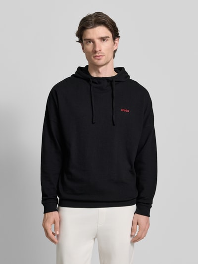 Męski model nosi Relaxed Fit Hoodie aus Baumwoll-Mix od HUGO, jednokolorowy, wyhaftowane logo, długi rękaw, wafel struktura, przód, ujęcie: Ganzkörperansicht von vorne.