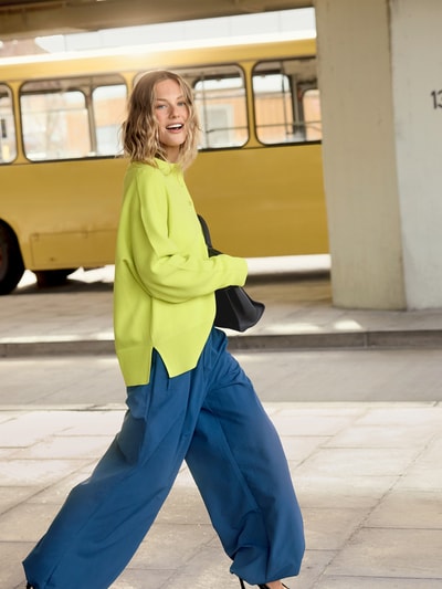Vrouwenmodel draagt 'Strick-Polohemd im Wide Fit - curated by Tinvcb' van SIC, geel met relaxed fit, polokraag, elastische mouwboorden, gebreide look, ruglengte 62 cm, mouwlengte 56 cm, vooraanzicht in volledige lengte