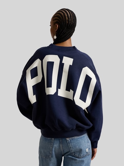 Vrouwenmodel draagt Oversized Sweatshirt aus Baumwoll-Mix von Polo Ralph Lauren in effen donkerblauw met groot wit logoprint, oversized fit, geribde boorden, sweat van katoenmix, label-print, lange mouwen, schouders verlaagd, rugaanzicht.