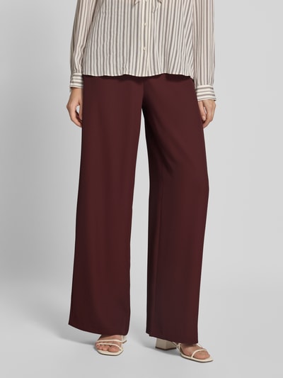Frauenmodel trägt Wide Fit Hose mit Gesäßtaschen von Jake*s aus elastischem Material-Mix, dunkelrot, fließende Textur, Nahaufnahme Unterkörper.