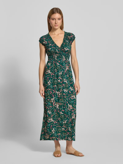Modelka nosi Regular Fit Maxikleid aus reiner Viskose mit V-Ausschnitt od Apricot, zielona z kwiatowym nadrukiem na całej powierzchni, krój regular fit, dekolt w serek, krótkie rękawy, obszycie falbanami, taliowany fason, plisy, długość tyłu w rozmiarze S 129 cm, szerokość w rozmiarze S 46 cm, widok całej sylwetki z przodu.