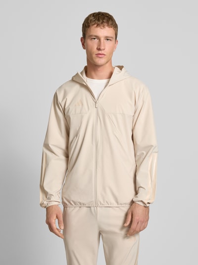 Männermodel trägt 'Trainingsjacke mit Kapuze' von adidas Sportswear in Beige, Regular Fit, Materialmix mit Stretch, Reißverschluss, Nahaufnahme Oberkörper.