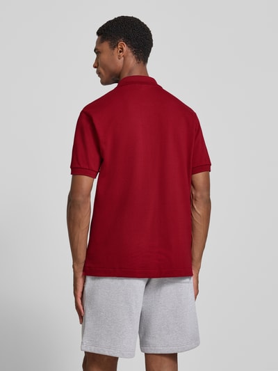 Mężczyzna model nosi czerwony koszulka polo Regular Fit Poloshirt aus reiner Baumwolle model 'CORE' von Lacoste na tle jasnym, całkowity widok od tyłu.