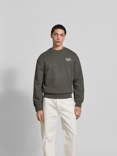 Männermodel trägt Sweatshirt aus Baumwoll-Mix von MAISON KITSUNÉ in Dunkelgrau mit Label-Stitching, lockerer Passform, Ganzkörperansicht von vorne