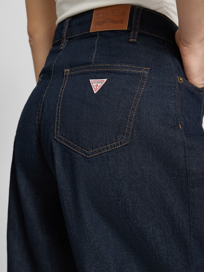 Frauenmodel trägt Bermudas im 5-Pocket-Design mit Label-Detail von Guess Jeans aus Reine Baumwolle, dunkles Blau, Detailaufnahme Gesäßtasche. Kontext: Damen Bermudas von Guess Jeans, Straight Fit, Knopf- und Reißverschluss, Bundweite bei Größe 27: 38 cm, Innenbeinlänge bei Größe 27: 31 cm.