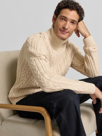 Męski model nosi Slim Fit Strickpullover mit Baumwoll-Anteil Modell 'Callum' od JACK & JONES Premium, kremowy sweter z dzianiny o splocie warkoczowym, długi rękaw, prążkowany golf i wykończenia, materiał mieszany, Ganzkörperansicht von vorne.