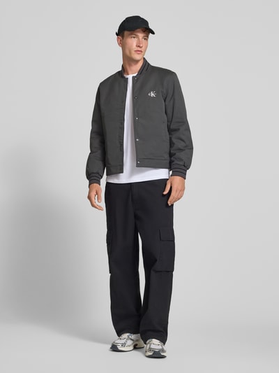 Männermodel trägt Relaxed Fit Bomberjacke aus reiner Baumwolle von Calvin Klein Jeans in Dunkelgrau, Herren Bomberjacke, Ganzkörperansicht von vorne.