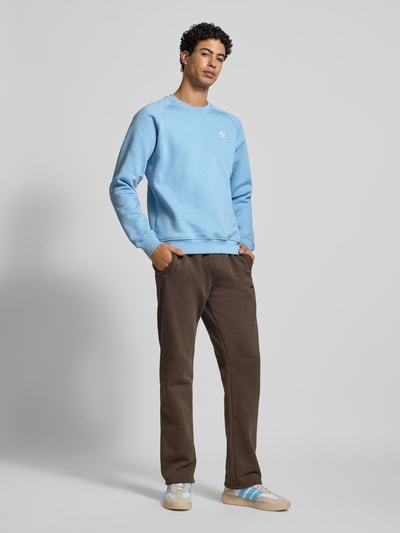 Männermodel trägt Sweatshirt mit Label-Stitching von adidas Originals in Hellblau aus Baumwoll-Mix, lockerer Schnitt, Gerippte-Abschlüsse, Rundhalsausschnitt; Rückenlänge 70 cm, Ärmellänge 82 cm, Ganzkörperansicht von vorne.