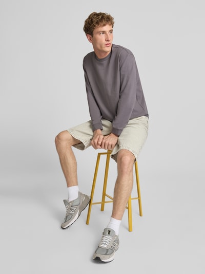 Männermodel trägt Loose Fit Langarmshirt aus reiner Baumwolle von Levi's® in Grau, kombiniert mit heller Shorts, Ganzkörperansicht von vorne.