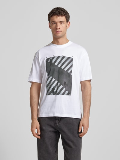 Männermodel trägt Slim Fit T-Shirt aus reiner Baumwolle Modell 'DODGER' von HUGO, Optik: Unifarben, Motiv-Print, Ganzkörperansicht von vorne.