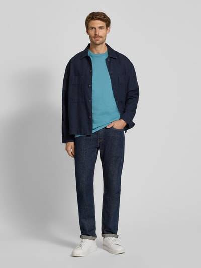 Männermodel trägt Regular Fit T-Shirt aus reiner Baumwolle von Scotch & Soda in Türkis, kombiniert mit Jeans und Jacke, Ganzkörperansicht von vorne. Rückenlänge bei Größe M: 61 cm, Logo-Stitching sichtbar, Rundhalsausschnitt.